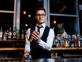 elegant young male barman prepares a delicious cocktail at the bar