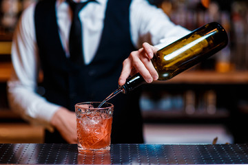 elegant young male bartender preparing a delicious cocktail at the bar. Bartender pours alcohol into a glass