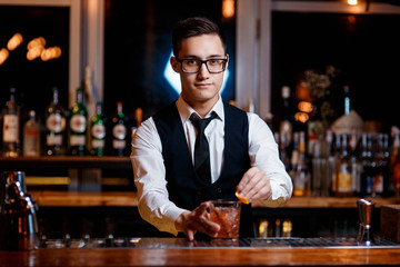 elegant young male bartender preparing a delicious cocktail at the bar. Bartender adds cinnamon