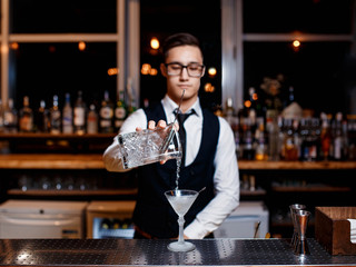 elegant young male barman prepares a delicious cocktail at the bar
