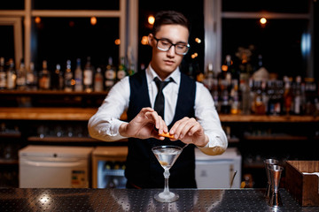 elegant young male barman prepares a delicious cocktail at the bar