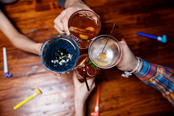 friends clinking by glasses with various alcoholic cocktails at table,close up top view
