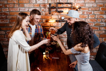 friends with smiles on their faces at the bar have fun, drink cocktails, cheks in glasses