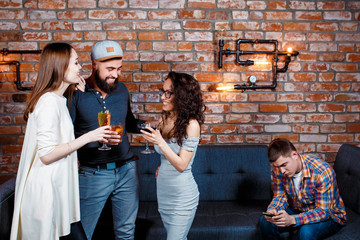 a guy at a party in a bar sits alone with a phone in his hand. alienated sociopath at a birthday party. dependence on the phone among the millennial youth. lack of communication in population Z.