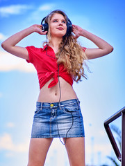 Student girl wearing in denim miniskirt and headphone listen music after exam. Time to relaxin street city.