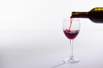 Red wine pouring from bottle into big glass on white background with copy space