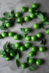 Green fresh organic plums on isolated background with blue and white cloth. On gray natural concrete background.