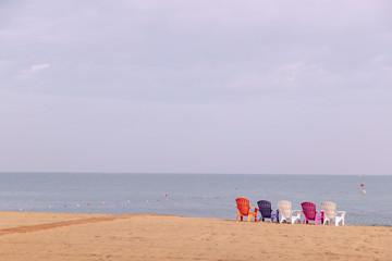 Fototapeta na wymiar A row of colored chairs on an empty beach by the sea. Background, plenty of space, horizontal, no people. Tourism concept.