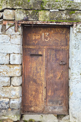 An old metal door with paint removed to a poor stone house.