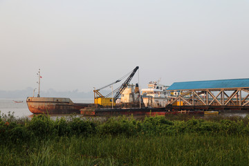 Fototapeta premium Crane on the ship with other ship moored at the harbor in river.