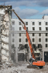 Building demolition excavator with long mechanical arm. Destruction of a house, reconstruction, bricks and metal, ruins, concrete dust in the air. Heavy machinery, hydraulic construction equipment.