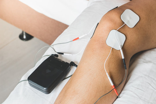 Patient applying electrical stimulation therapy on knee joint. Therapist placing electrodes on Knee. Electrical tens.