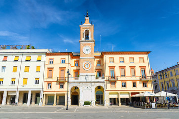 Traditional building with clock and bell tower on Piazza Tre Martiri Three Martyrs square in old historical touristic city centre Rimini with blue sky background, Emilia-Romagna, Italy
