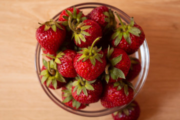 Beautiful, ripe red strawberries shot from above in a glass saucer on a worn white background.