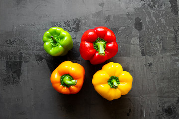 Green, orange, red and yellow fresh organic peppers on isolated background with blue and white cloth. On gray natural concrete background.