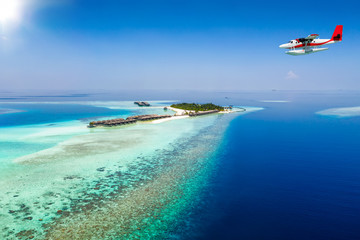 Wasserflugzeug fliegt über eine Insel auf den Malediven im Indischen Ozean mit türkisem Wasser...