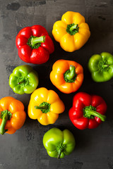 Green, orange, red and yellow fresh organic peppers on isolated background with blue and white cloth. On gray natural concrete background.
