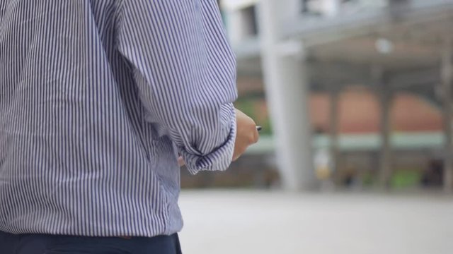 Close up asian businessman walking and using smartphone. Asian man with glasses use phone in street near big office building.