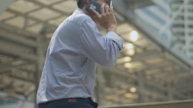 Asian businessman walking and using smartphone. Slow motion portrait asian businessman answers the phone. Asian man with glasses use phone in street near big office building.