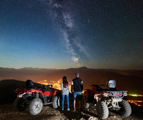 Rear view of boy and girl tourists with two atv quad motorbikes on the top of mountain, romantic...