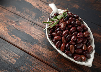 Pitted kalamata olives in bowl on rustic wooden background