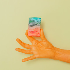 Pastel colors Natural Luxury. Painted hand holds soap slice with marbleized effect. Bright and soft yellow background. Minimal and aesthetic