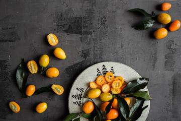 Orange fresh organic kumquats on isolated background with blue and white cloth. Citrus fruit sour and sweet cumquats. On gray natural concrete background.