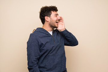 Man with curly hair over isolated wall shouting with mouth wide open to the lateral