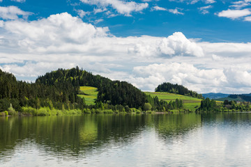 Serene landscape with green hills at lake, summer sunny day with clouds over blue sky