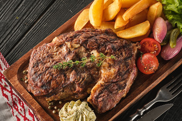Ribeye steak with potatoes, onions and baked cherry tomatoes. Juicy steak with flavored butter