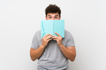 Man with curly hair over isolated wall holding and reading a book