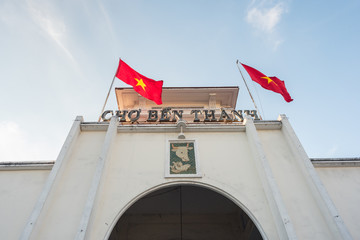 Ben Thanh Market (built in 1912-1914), the facade and the arch of the central entrance and two swaying Vietnamese flags. The market is one of the top attractions of Ho Chi Minh City (Saigon), Vietnam.