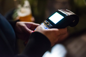 Cropped view of womens hand using credit card to make payment on Payment terminal in bar 