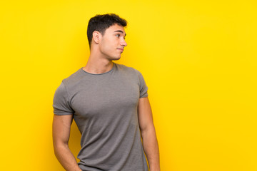 Obraz premium Handsome man over isolated yellow wall making doubts gesture looking side