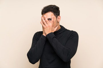 Handsome man over isolated background covering eyes and looking through fingers