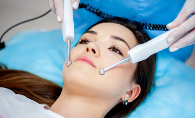 Fototapeta premium cosmetologist with a patient during facial procedures in a modern cosmetological and aesthetic clinic. A patient receives an electric facial massage. Skin rejuvenation and wrinkle smoothing.