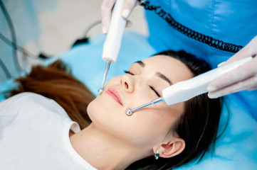 Fototapeta premium cosmetologist with a patient during facial procedures in a modern cosmetological and aesthetic clinic. A patient receives an electric facial massage. Skin rejuvenation and wrinkle smoothing.