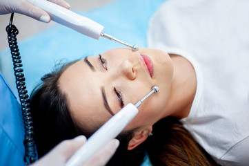 cosmetologist with a patient during facial procedures in a modern cosmetological and aesthetic clinic. A patient receives an electric facial massage. Skin rejuvenation and wrinkle smoothing.