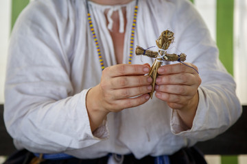 Woman in Russian ethnic clothes makes a small toy of straw