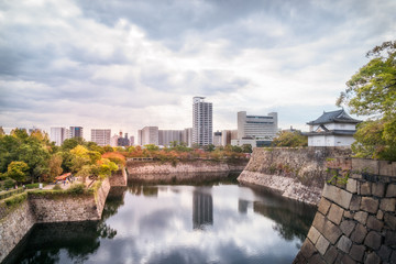 Fototapeta na wymiar Reflections in the water at Osaka Castle Park Moat and outerwall with Osaka cityscape in the distance in Japan.