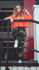 Fashion model wearing red hoodie with the inscription los angeles posing in the city at parking. Fashion urban outfit. Casual everyday clothing style