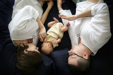 Obraz na płótnie Canvas Newborn between parents on dark sheet, dad and mom