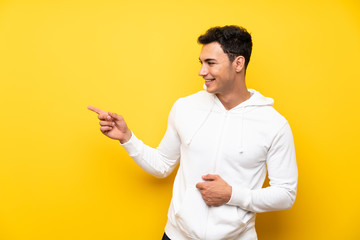 Handsome man over isolated yellow wall pointing to the lateral