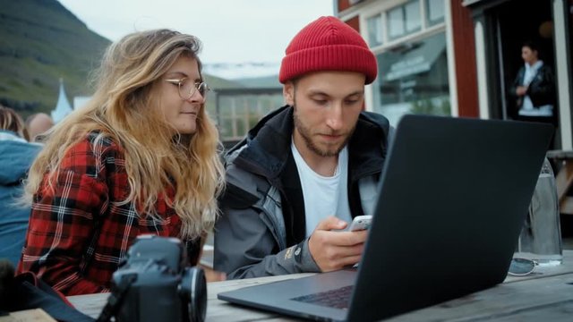 Two young professionals from creative industry have casual outside of office meeting. Discuss business startup idea over laptop on table. Comment and share ideas and plans for collaboration
