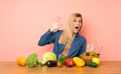 Young blonde woman with many vegetables nervous and scared