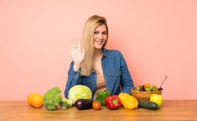 Young blonde woman with many vegetables counting five with fingers