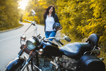 Plakat attractive brunette motorcyclist standing near a motorcycle On the Sunset. adventure concept