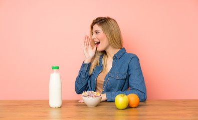 Young blonde woman with bowl of cereals shouting with mouth wide open