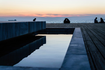 People sitting in the pier in Thessaloniki, Greece. Watching the sunset and talking to each other