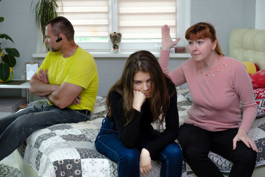 Photograph of the problems, the conflict of a disgruntled, swearing father, mother and brunette girl with long dark hair in the room. They are sitting on the sofa and are unhappy.